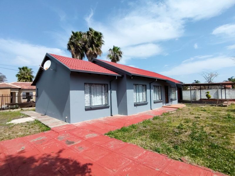 A single-story residential house featuring a red tiled roof, grey exterior walls, security window bars, and a paved walkway leading to the entrance.