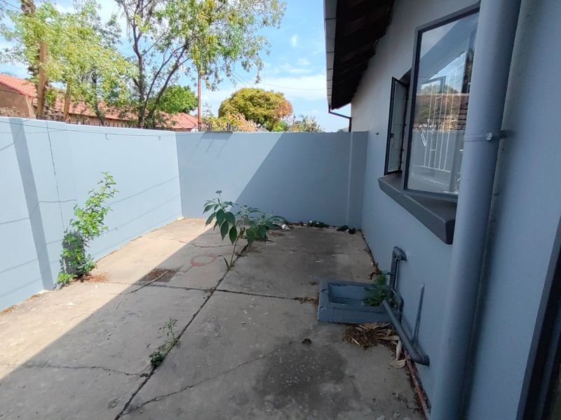 A private rear courtyard area featuring concrete paving, a boundary wall, and external utility plumbing, offering potential for landscaping or outdoor improvement.