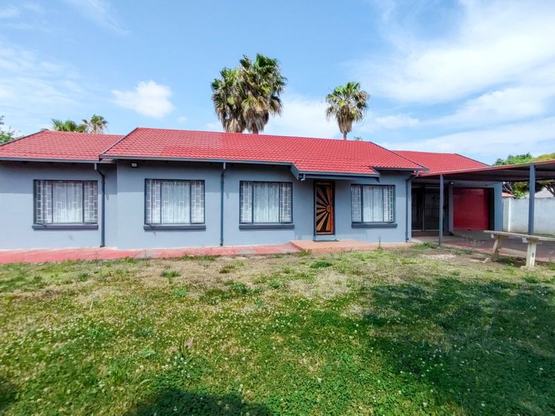 Front view of a single-story house featuring a red metal roof, security window bars, and an attached carport with a garage.
