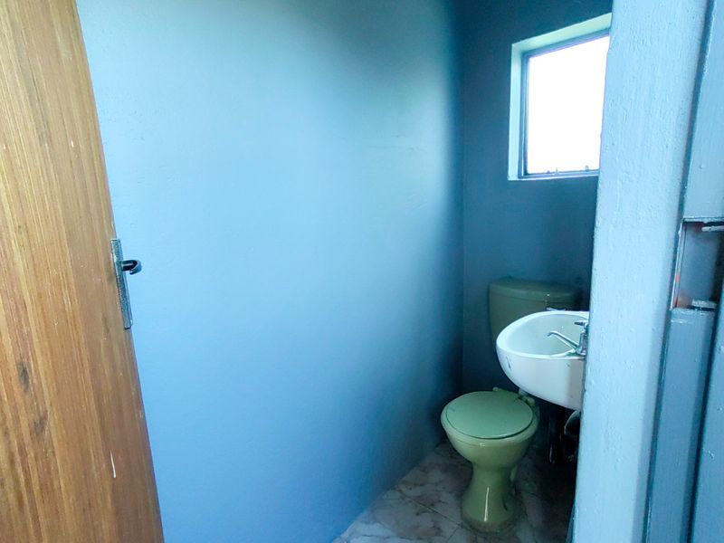 A compact bathroom featuring a wall-mounted basin and toilet, requiring cosmetic updates to modernize the space.