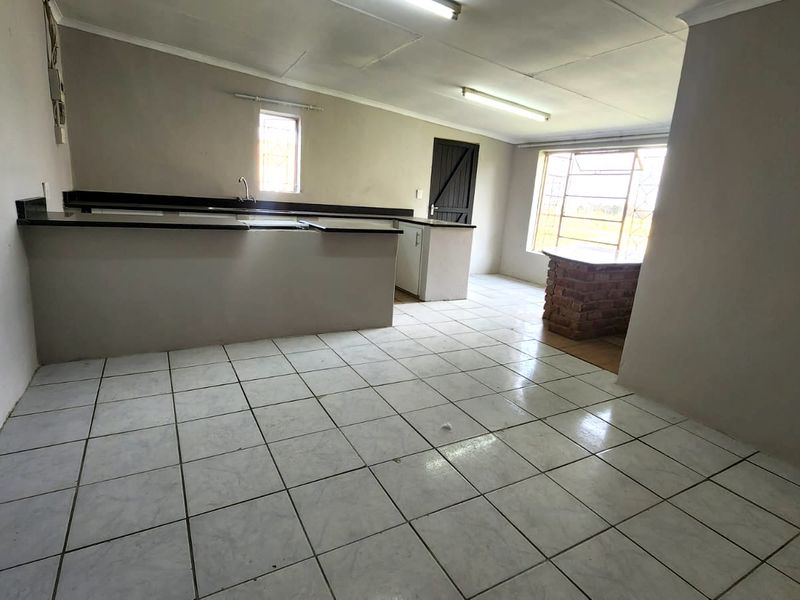 An empty, open-plan kitchen area featuring tiled flooring, built-in cabinetry, a sink, and a unique brick breakfast bar, ready for renovation.