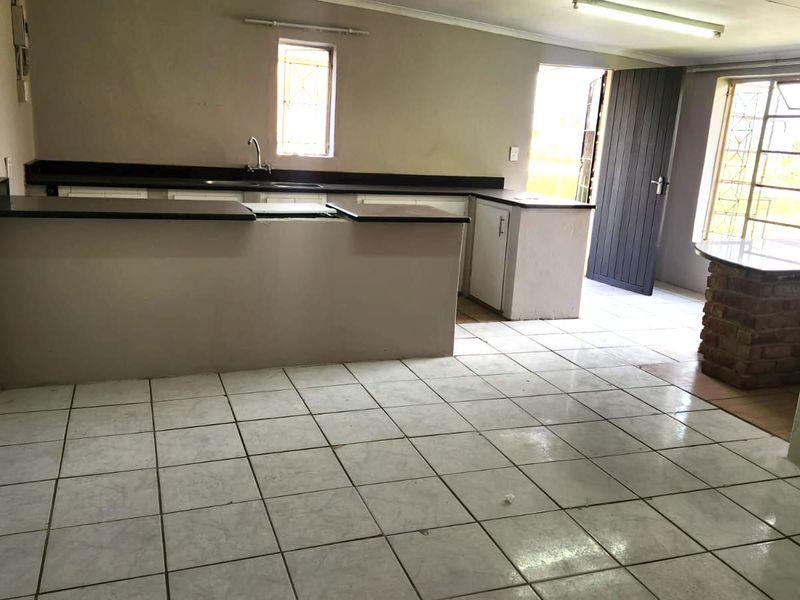 An empty kitchen featuring tiled flooring, built-in cabinetry with countertops, a brick breakfast bar, and direct access to the exterior.