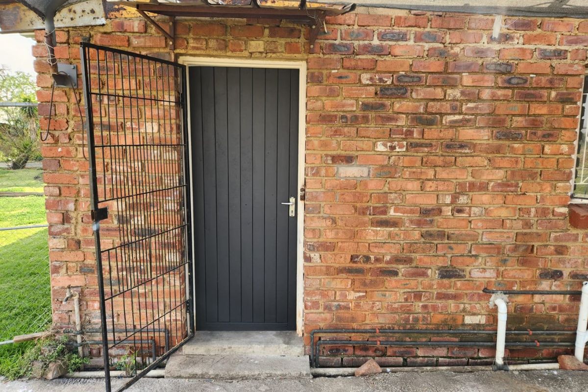Rear exterior view showing a brick wall, security gate, and external door with exposed plumbing fixtures.