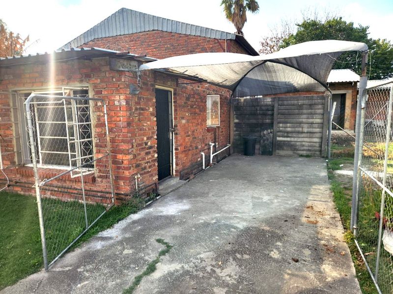 Rear exterior view of a brick house featuring a concrete driveway, shade cloth carport, and security fencing.