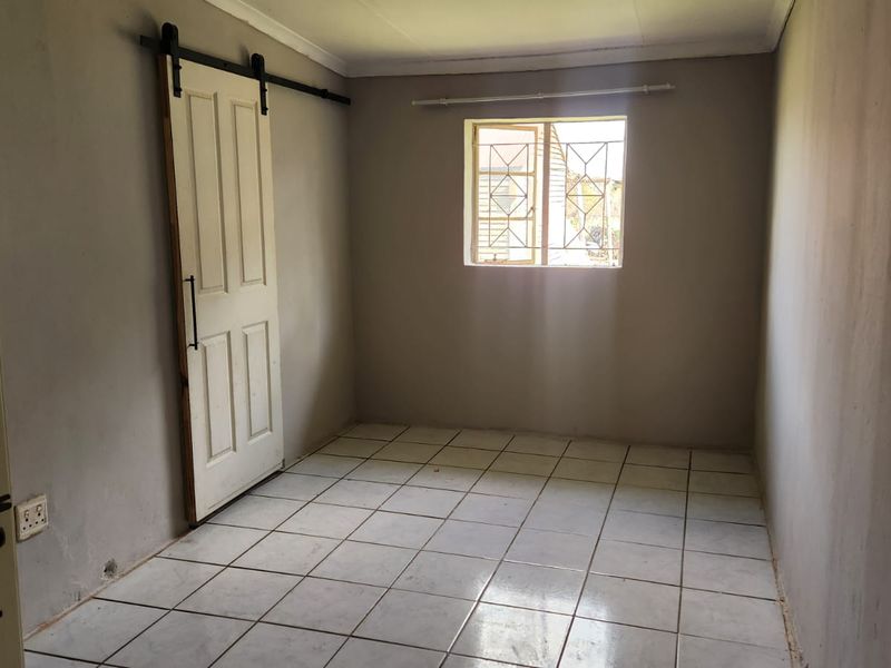 An empty bedroom featuring ceramic tiled flooring, a sliding barn-style door, and a window fitted with security bars.