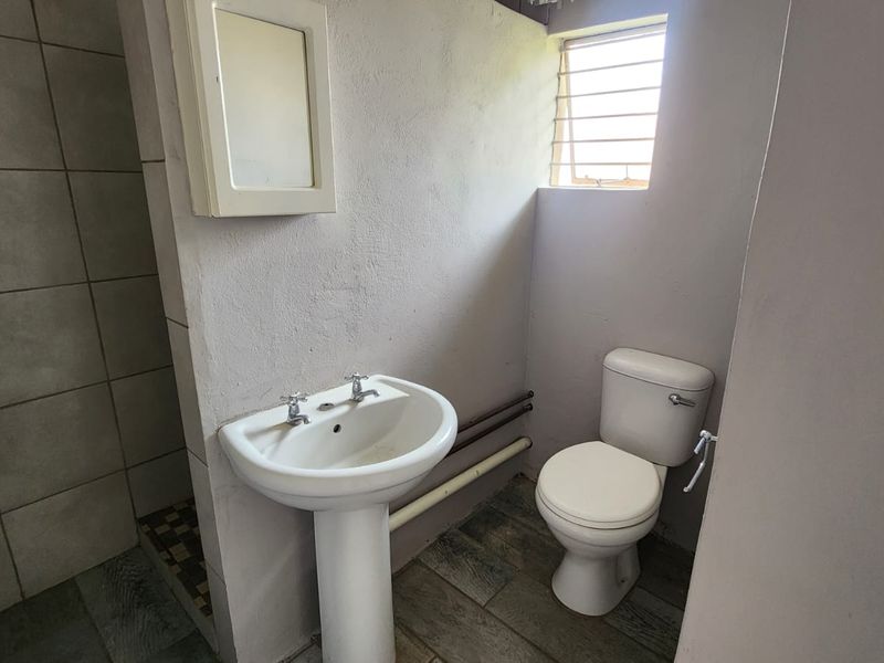 A functional bathroom featuring a pedestal basin, toilet, and shower enclosure with tiled flooring and exposed plumbing elements.
