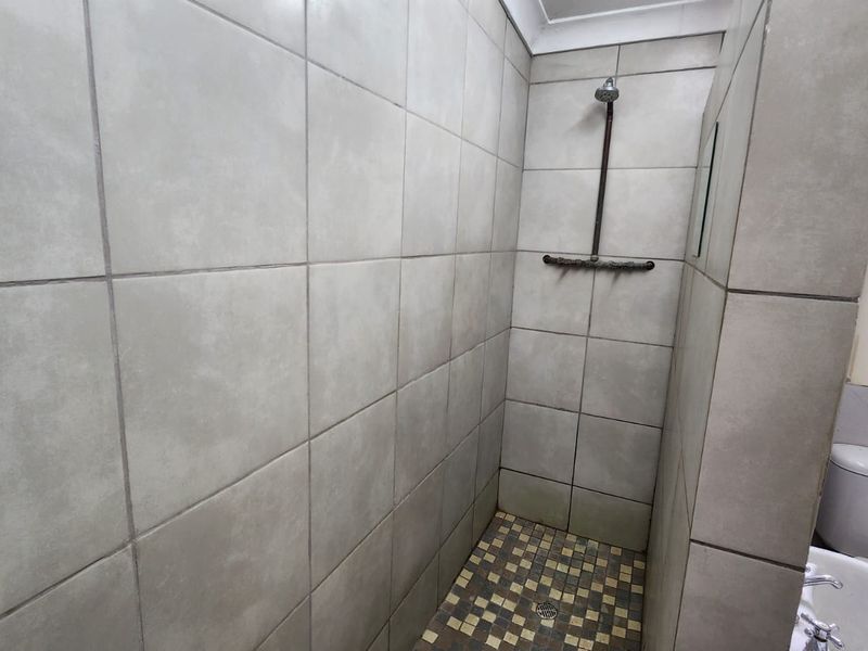 A functional bathroom featuring a tiled shower enclosure with exposed plumbing, a standard toilet, and a basin.