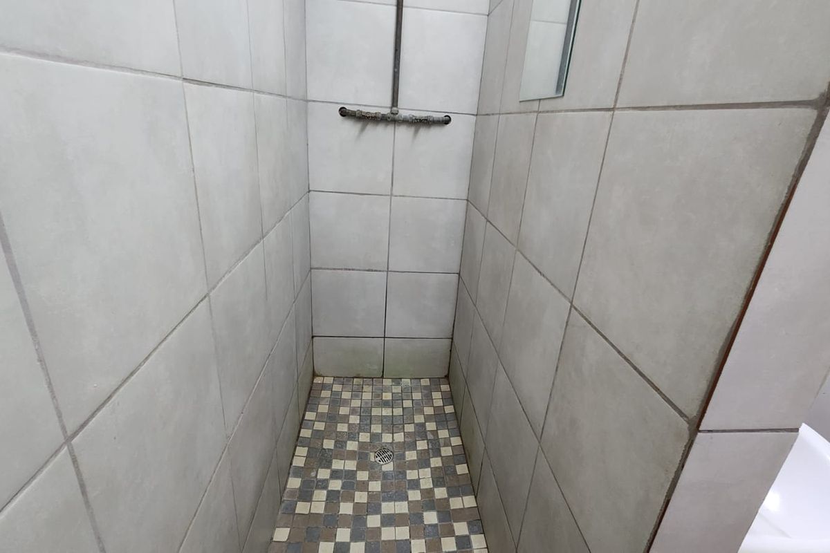 A compact shower stall featuring neutral wall tiles, a mosaic floor pattern, and exposed shower plumbing.