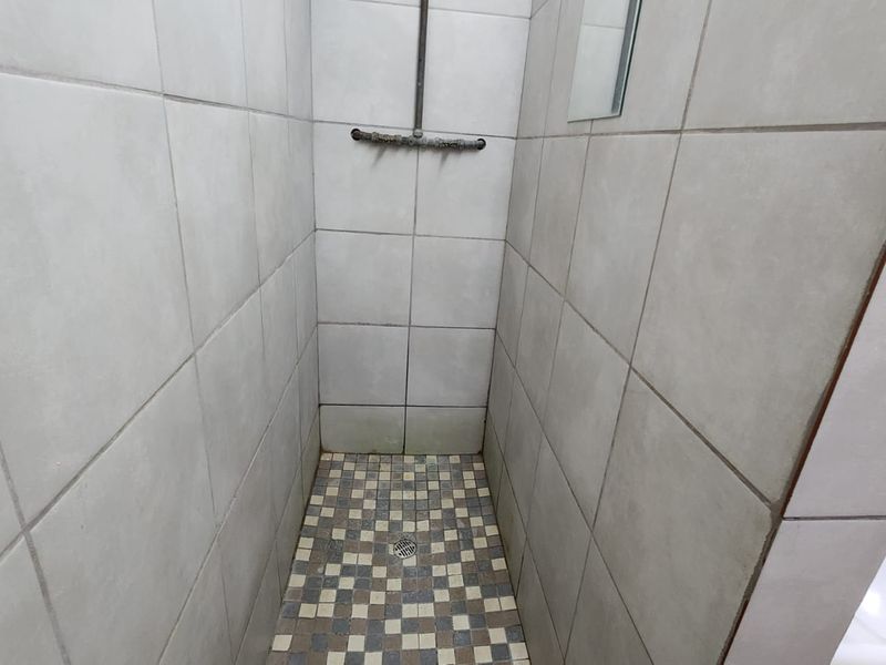 A compact shower stall featuring neutral wall tiles, a mosaic floor pattern, and exposed shower plumbing.