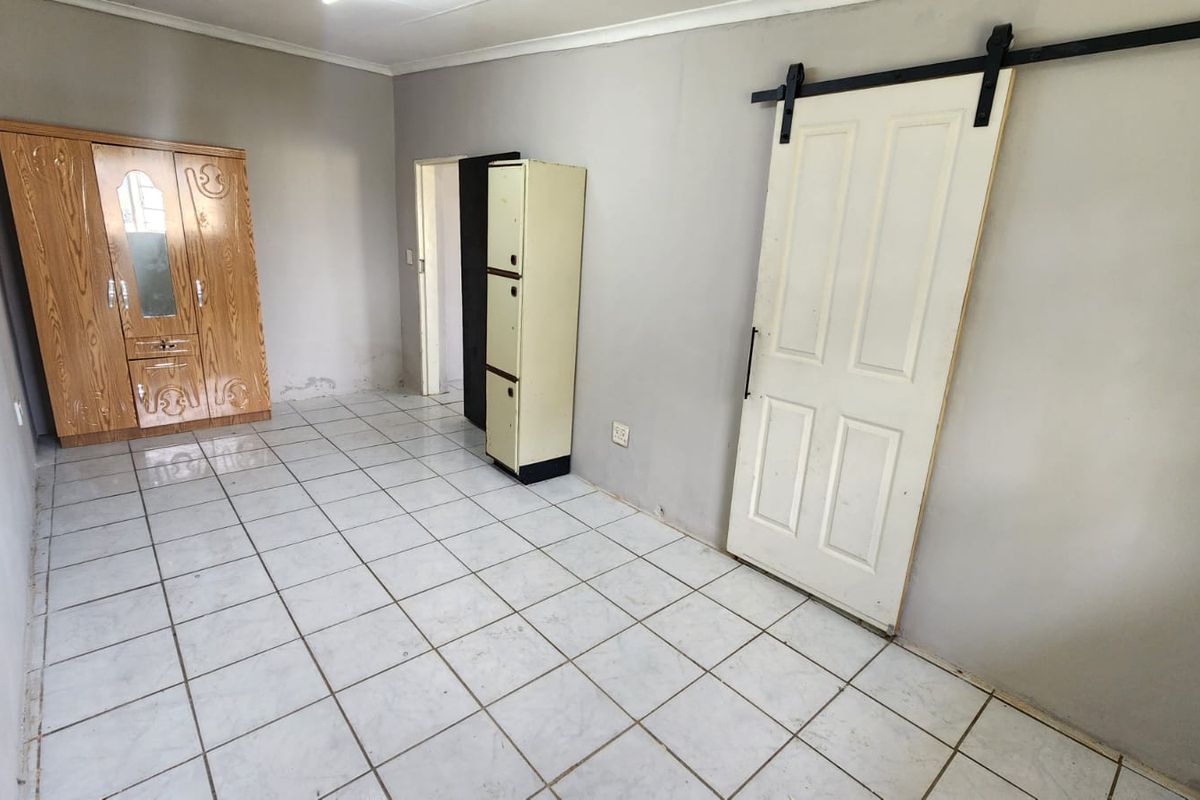 A spacious bedroom featuring white tiled flooring and a modern sliding barn door, offering a blank canvas for personalization.