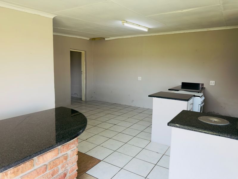 An empty kitchen featuring granite countertops, a brick breakfast bar, and tiled flooring, offering a functional layout ready for modernization.