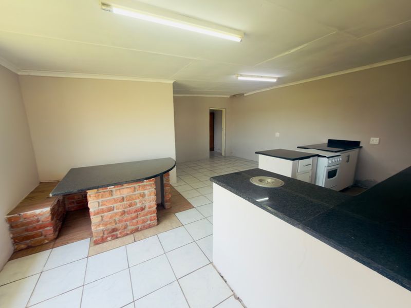 An empty kitchen featuring granite countertops, a brick breakfast bar, and ceramic tile flooring, awaiting modern updates and finishing touches.