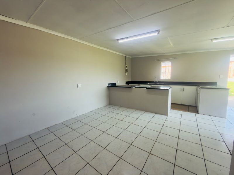 An empty kitchen featuring tiled flooring, built-in cabinetry with granite countertops, and a single sink, offering a blank canvas for potential updates.