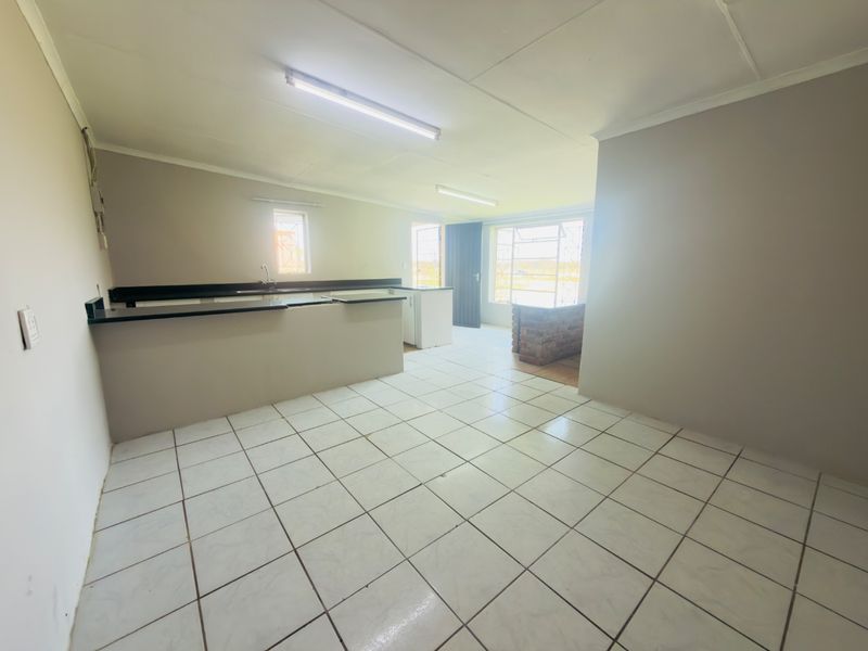 An open-plan living and kitchen area featuring tiled flooring, a built-in counter, and large windows with security bars.