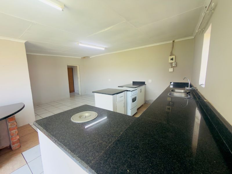 An empty kitchen featuring granite countertops, a double basin sink, and a freestanding stove, requiring cosmetic updates and electrical maintenance.