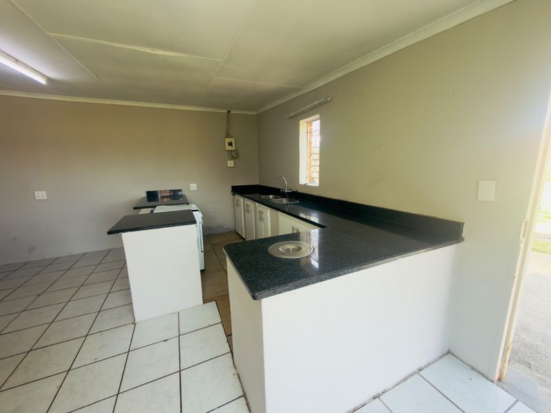 A functional, empty kitchen featuring granite countertops, built-in cabinetry, and tiled flooring, offering a blank canvas for potential updates.
