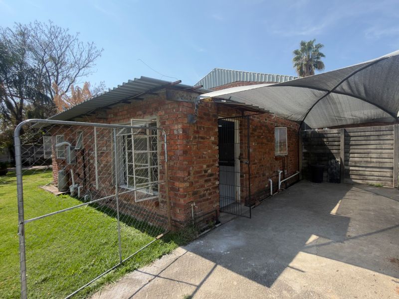 Rear exterior view of a brick house featuring a concrete driveway, shade cloth carport, and security features on windows and doors.