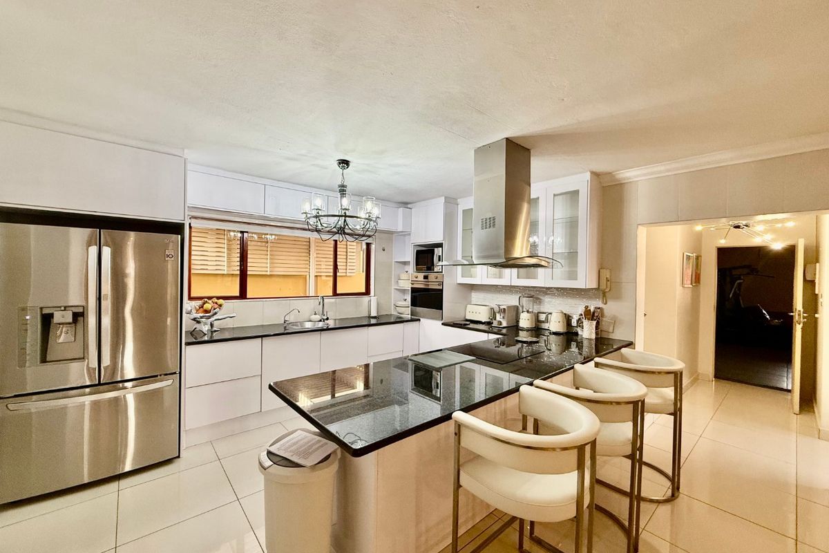 Modern kitchen featuring sleek white cabinetry, contrasting granite countertops, a central island with breakfast bar seating, and high-quality built-in appliances.