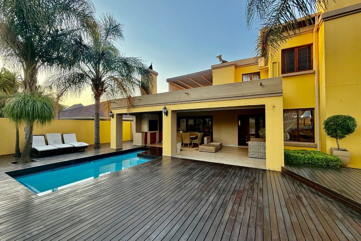 Rear exterior view featuring a swimming pool, extensive timber decking, and a covered patio area with a built-in braai.