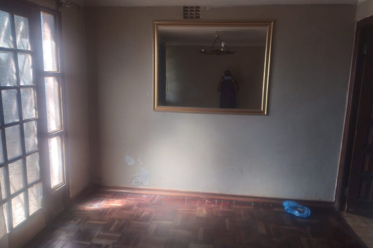 An empty living room featuring traditional parquet flooring, a timber-framed glass door, and visible wall surface wear requiring maintenance.