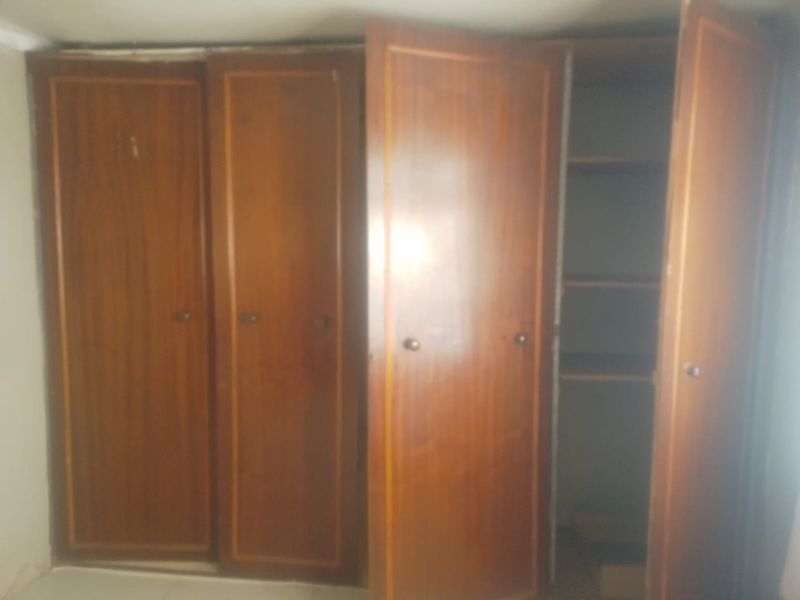 A bedroom featuring dated built-in wooden wardrobes with shelving, showing signs of wear and requiring cosmetic updates.