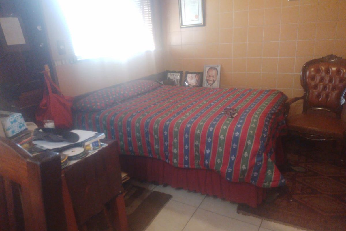 A bedroom featuring tiled walls and flooring, with natural light entering through a window fitted with venetian blinds.