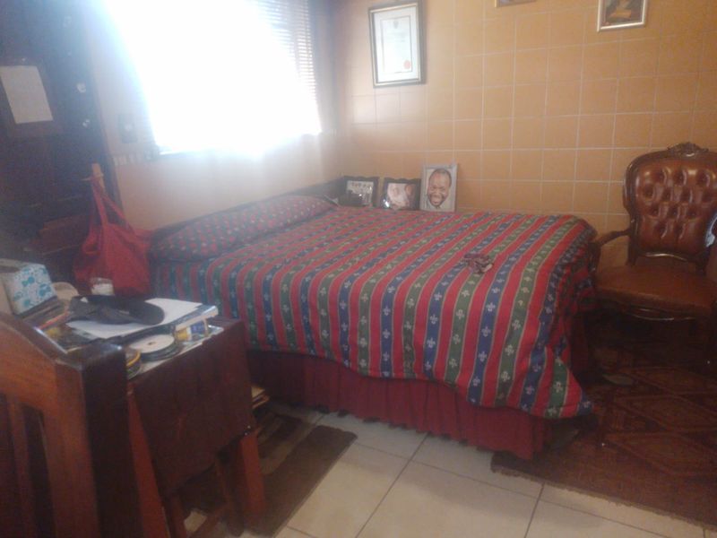 A bedroom featuring tiled walls and flooring, with natural light entering through a window fitted with venetian blinds.