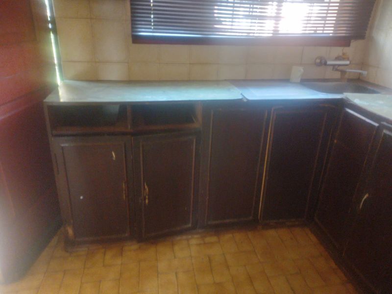 A dated kitchen area featuring worn built-in cabinetry, a stainless steel sink, and tiled finishes, requiring renovation to modernize the space.