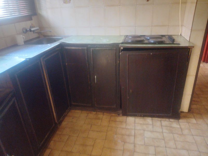 A dated kitchen featuring dark built-in cabinetry, a stainless steel sink, and an integrated electric hob with tiled backsplash and flooring.