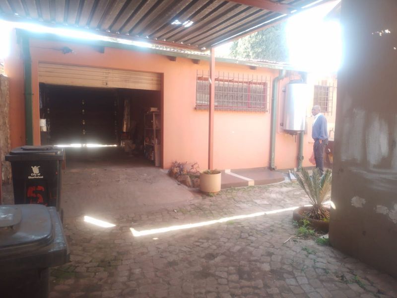 Rear exterior view showing a garage, paved courtyard area, and external geyser installation with security bars on windows.