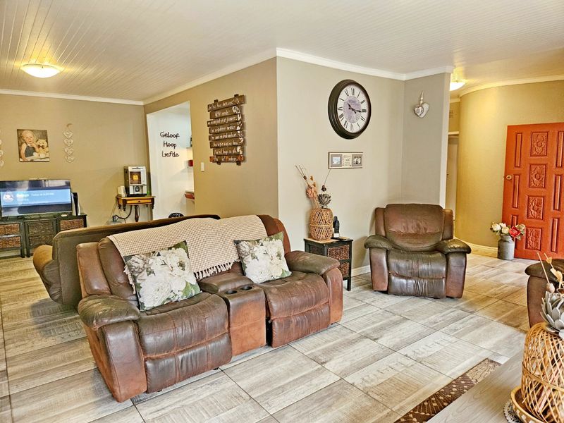 A spacious living area featuring light-toned tiled flooring, a beadboard ceiling with coving, and a distinctive solid wood entrance door.