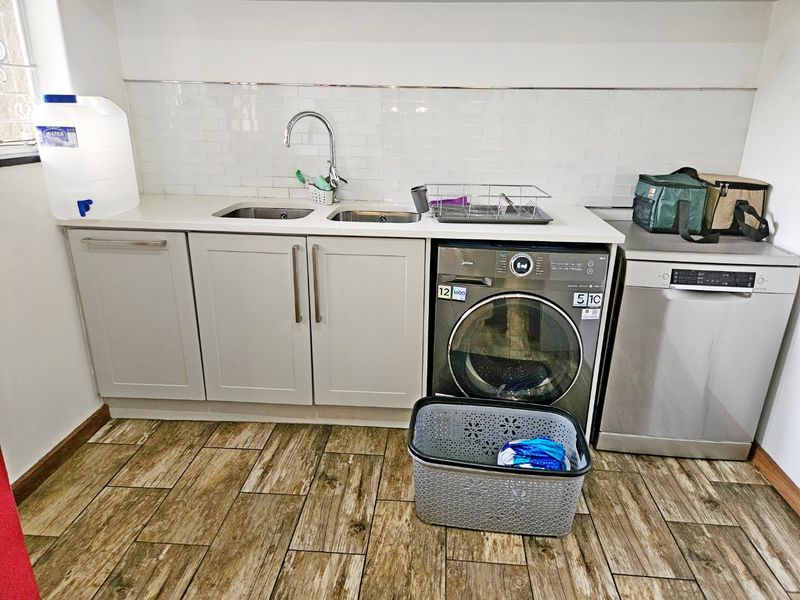 A functional laundry area featuring built-in cabinetry, a double sink with chrome tapware, subway tile backsplash, and durable wood-look tile flooring.