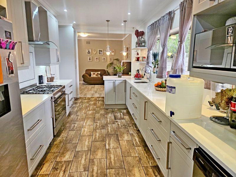 Modern open-plan kitchen featuring shaker-style cabinetry, quartz countertops, gas cooktop, and wood-look tiled flooring, flowing into an adjacent living area.