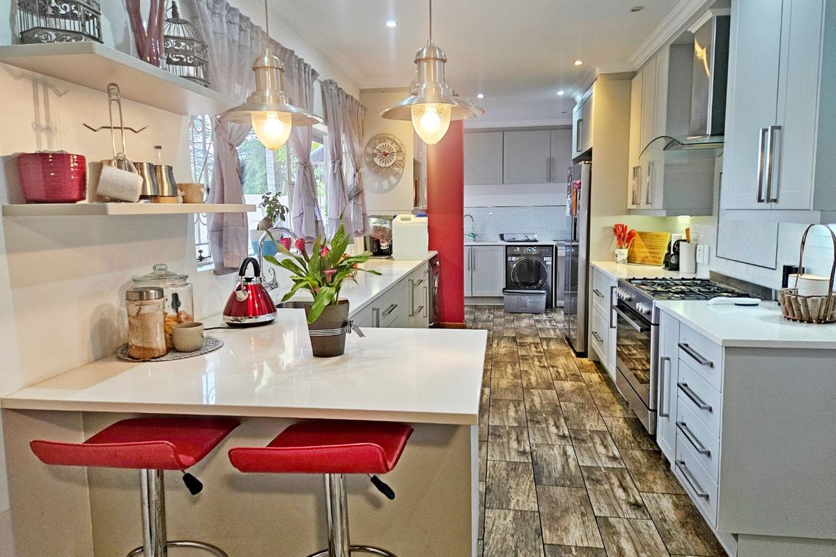 Modern kitchen featuring quartz countertops, gas hob, built-in oven, and wood-look tiled flooring with a breakfast bar and integrated scullery area.