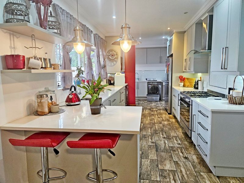 Modern kitchen featuring quartz countertops, gas hob, built-in oven, and wood-look tiled flooring with a breakfast bar and integrated scullery area.