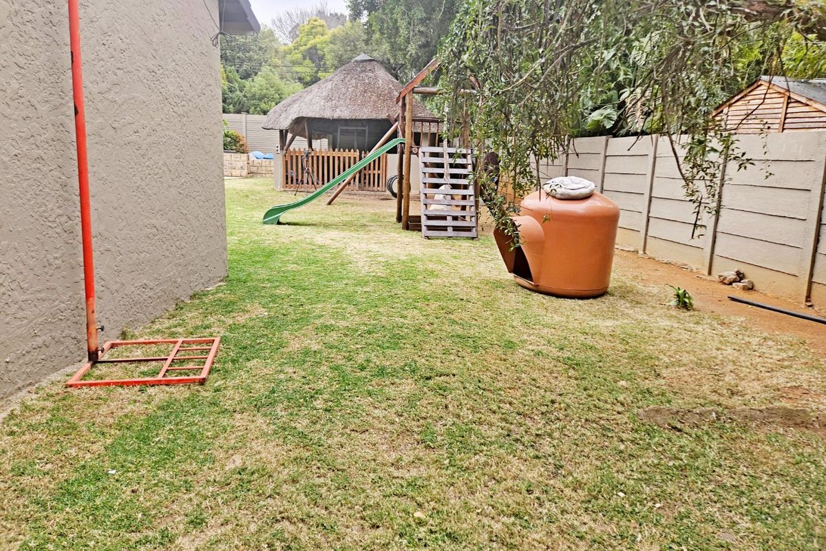 A rear garden area featuring a lawn, a thatched lapa structure, and a precast concrete boundary wall.