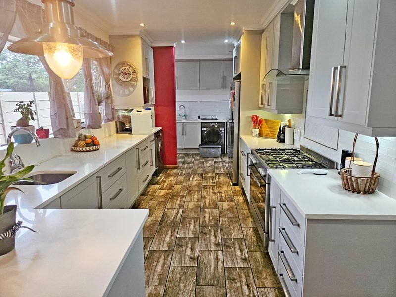 Modern kitchen featuring shaker-style cabinetry, quartz countertops, gas hob, built-in oven, and wood-look tiled flooring, with an adjoining scullery area.