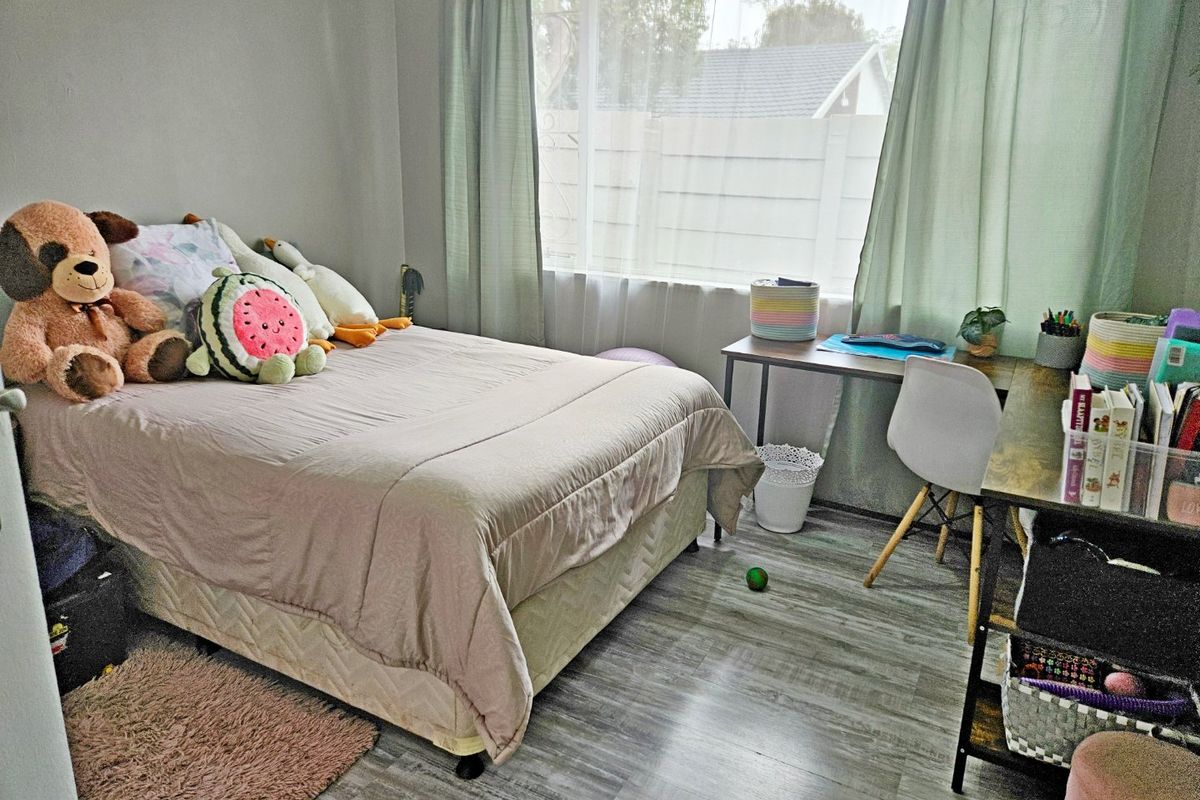 A functional bedroom featuring light-toned laminate flooring and a large window that provides natural light.