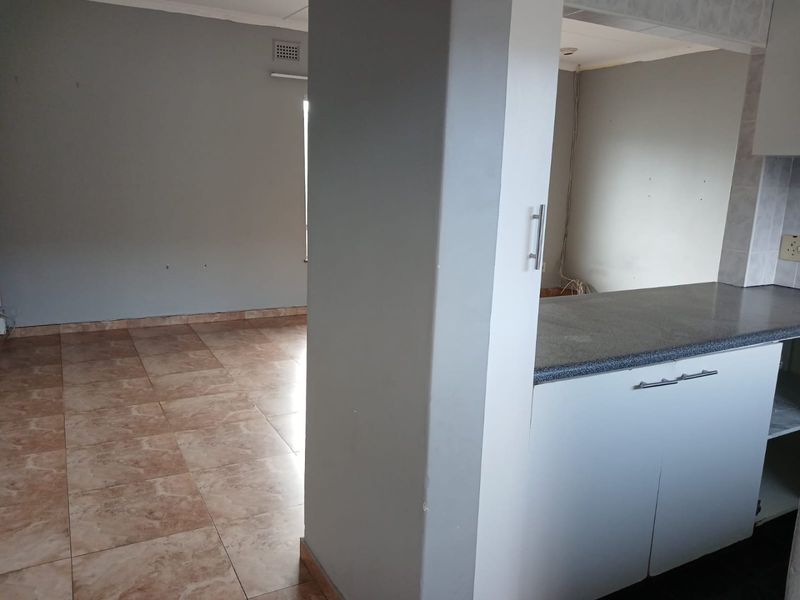 An empty open-plan living and kitchen area featuring tiled floors, built-in cabinetry, and a central structural pillar, requiring minor cosmetic updates.