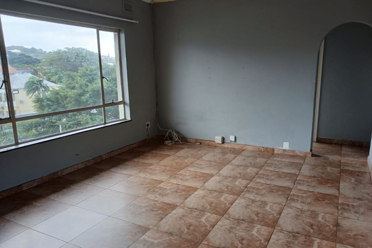 An empty living room featuring large windows with a view, tiled flooring, and an arched entryway leading to another area of the apartment.