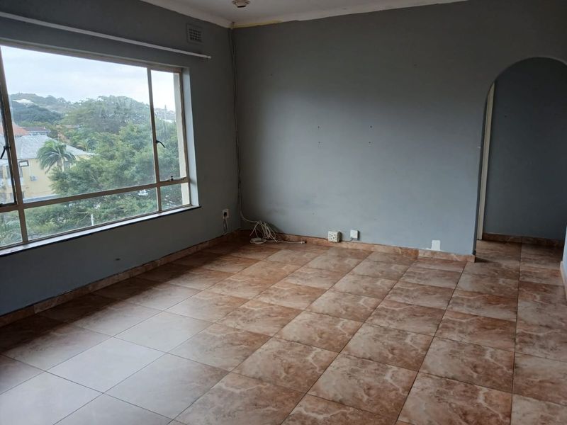 An empty living room featuring large windows with a view, tiled flooring, and an arched entryway leading to another area of the apartment.