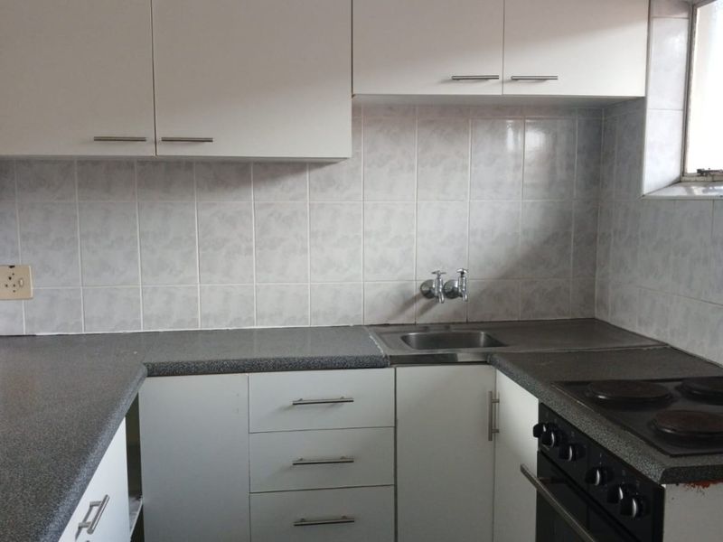 A functional kitchen featuring white built-in cabinetry, grey laminate countertops, a stainless steel sink, and a built-in electric stove and oven.