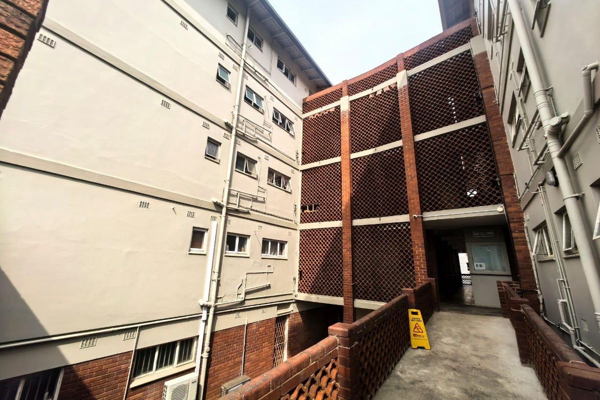 Exterior view of an apartment building complex featuring brick masonry, decorative breeze block screening, and a concrete walkway connecting the units.