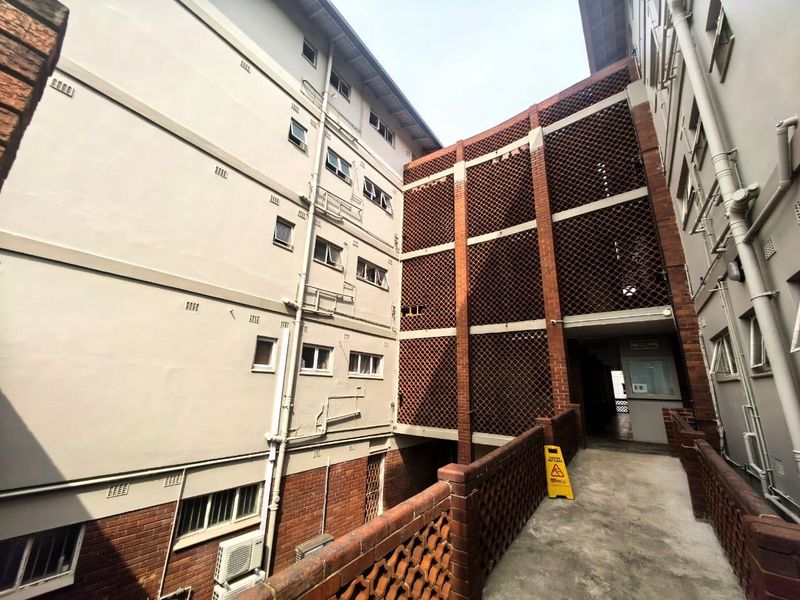 Exterior view of an apartment building complex featuring brick masonry, decorative breeze block screening, and a concrete walkway connecting the units.
