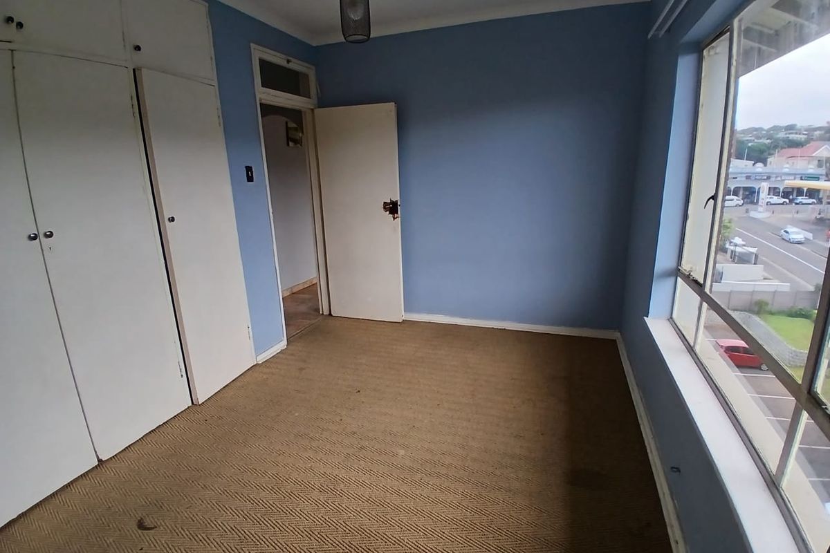 An empty bedroom featuring built-in cupboards, carpeted flooring, and a large window with views of the street.