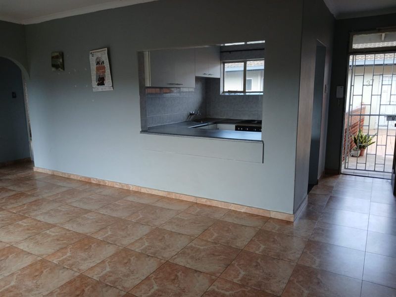 Open plan living area featuring tiled flooring and a convenient pass-through window connecting to the kitchen, with direct access to an exterior security gate.