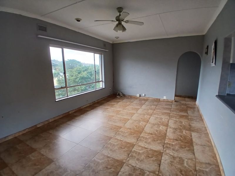 An empty living room featuring tiled flooring, a ceiling fan, and an arched entryway, offering a blank canvas for interior design.