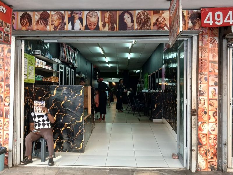 Street-level commercial storefront featuring a tiled entrance, reception counter, and interior salon space with fluorescent lighting.
