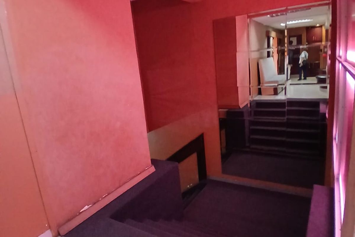 A commercial hallway featuring a carpeted staircase, tiled flooring, and a large mirrored wall panel with dated red wall finishes.