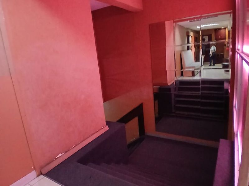 A commercial hallway featuring a carpeted staircase, tiled flooring, and a large mirrored wall panel with dated red wall finishes.